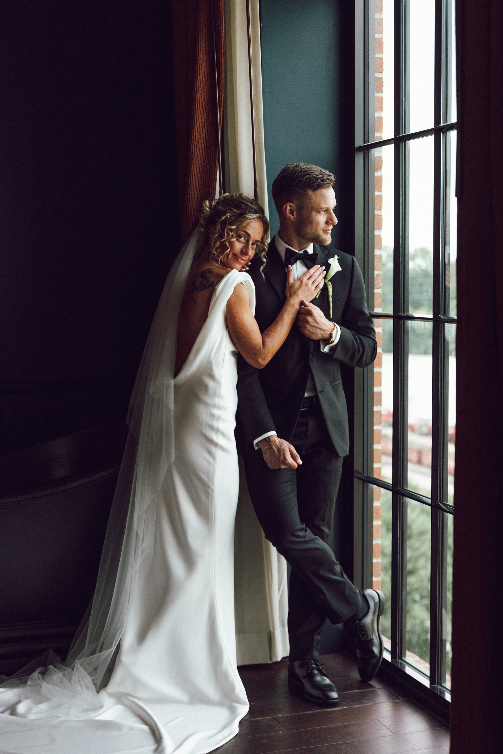 Couple leaning together beside floor-to-ceiling windows