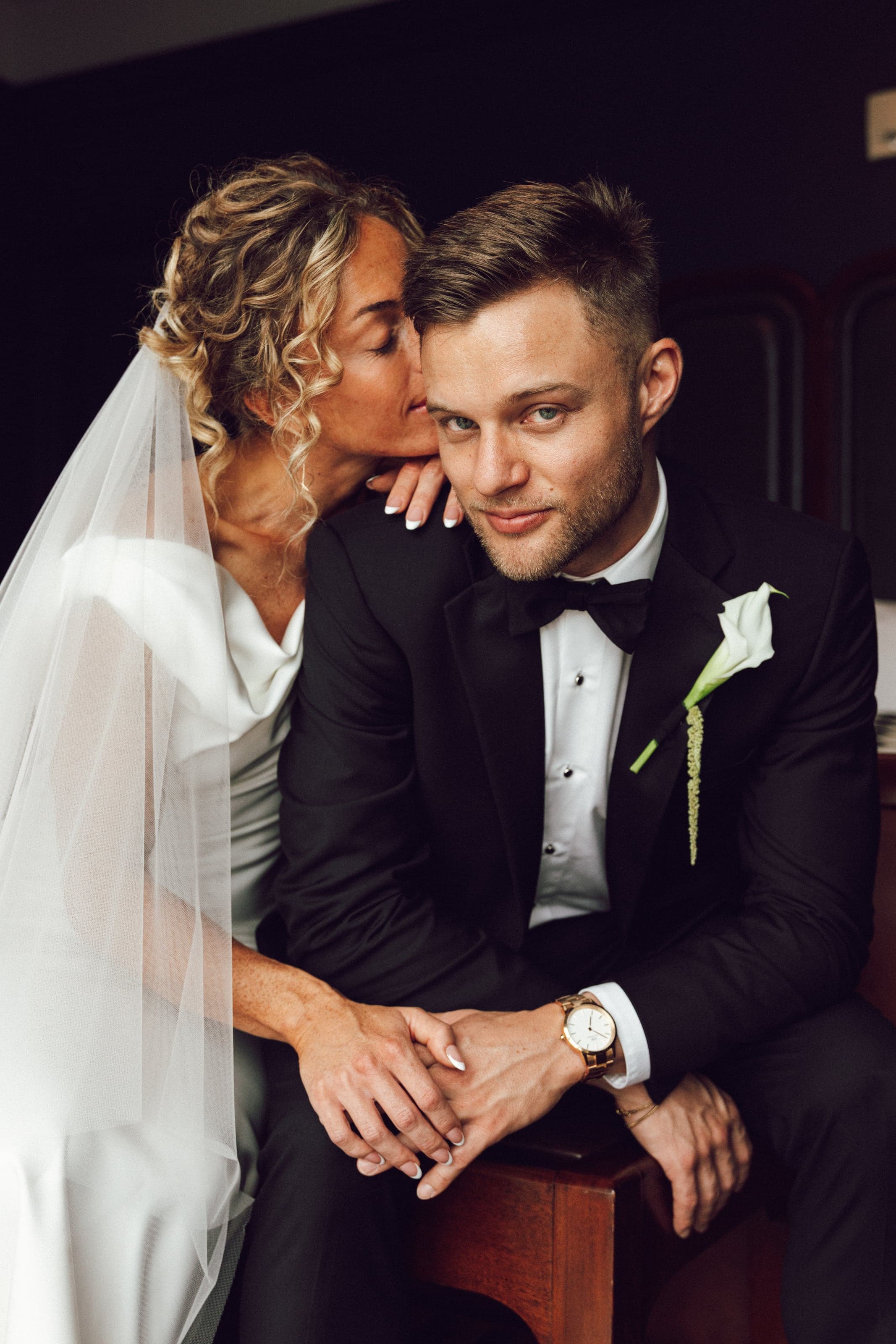 Bride kissing the groom’s cheek as he looks at the camera
