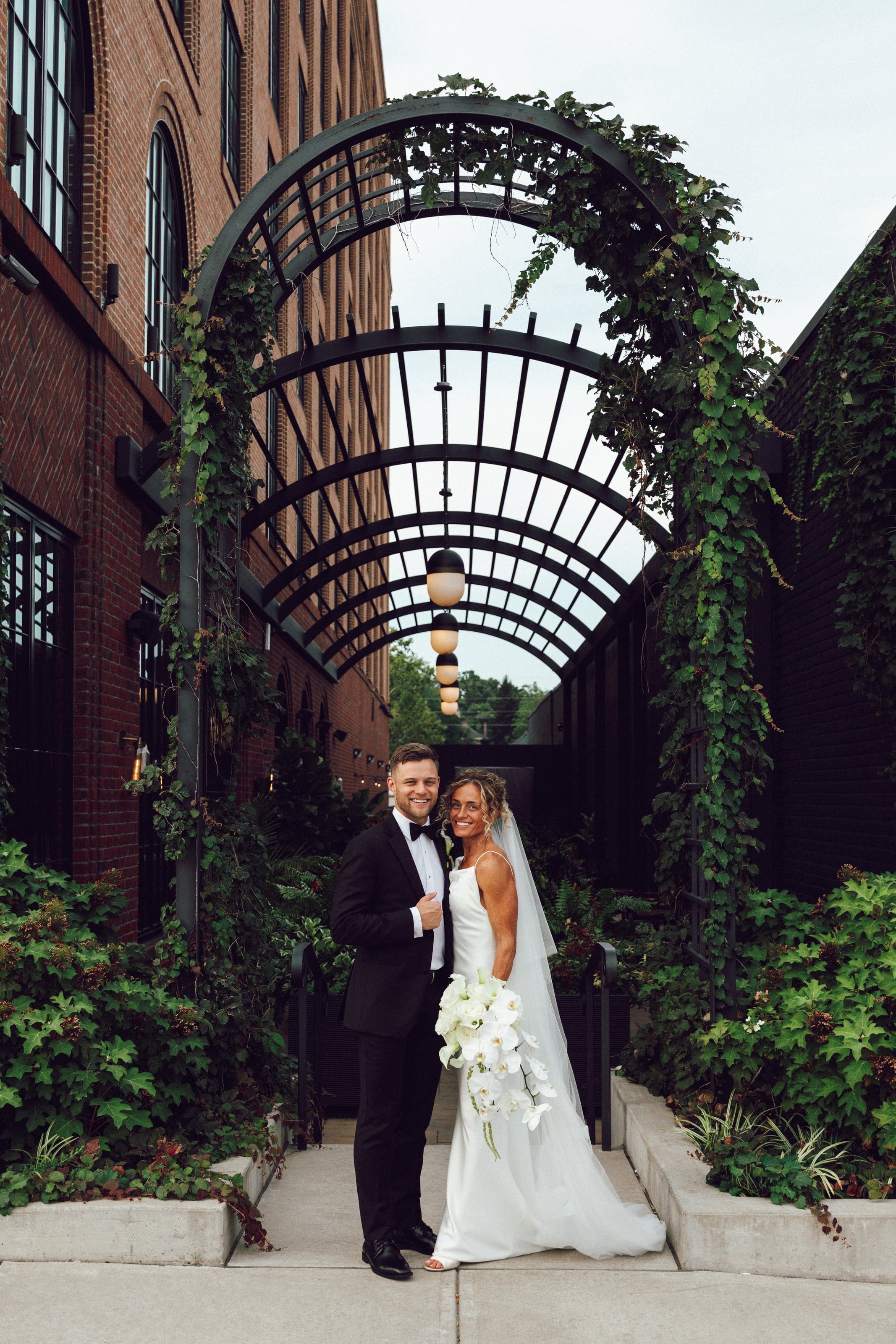 Couple under a green iron archway between brick buildings