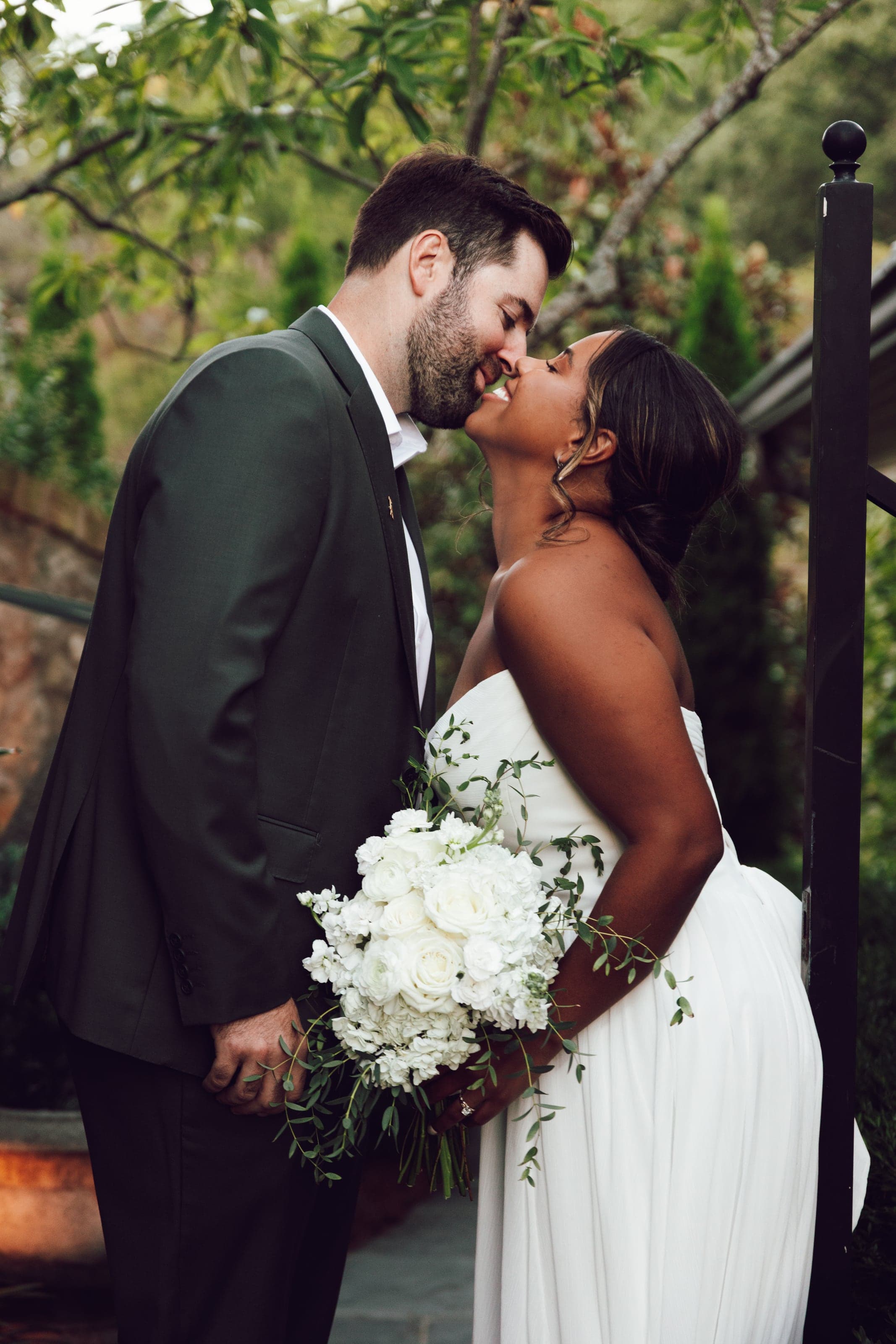 Couple kissing among trees, bouquet in hand
